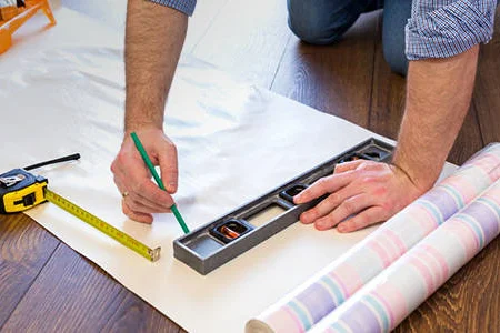 Person misst Tapete mit Zollstock und Wasserwaage aus